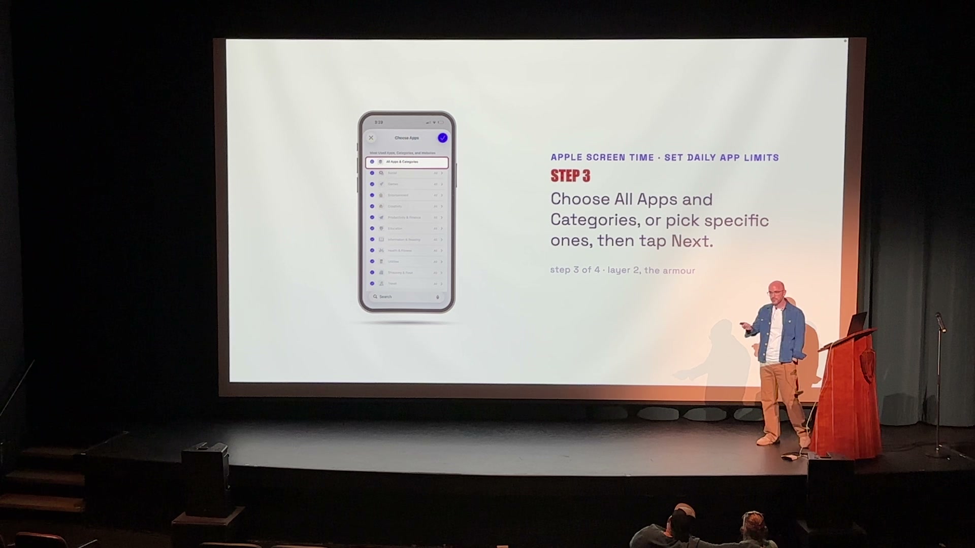 Colin on the Creekside Theatre stage, a Safe Family Internet slide filling the screen behind him: a purple phone frame showing an iPhone Screen Time setting, with the step written in plain language beside it.